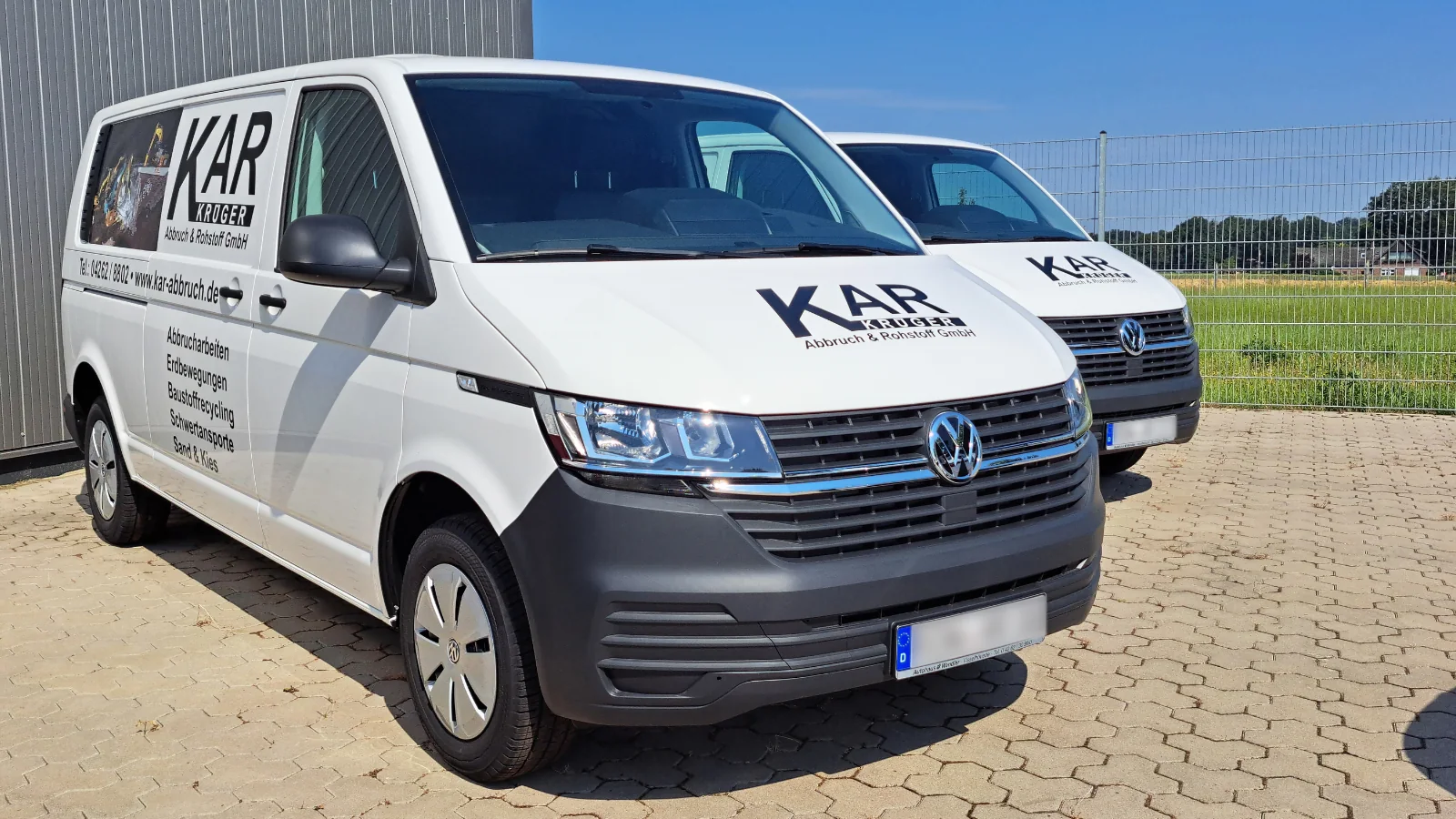 Zwei weiße Transporter mit einheitlicher Firmenbeschriftung auf Motorhaube und Seite